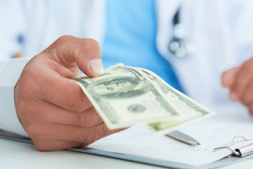 Male medicine doctor's hand holding two hundred dollars banknotes closae-up. Medic personnel salary, prestige and high paid job, education, public health business, medical insurance concept. - 211503068