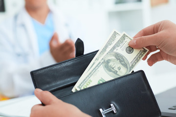 Female patient takes out of her wallet hundred dollar bills to pay for the services of a doctor. Bribery and corruption in Health Care Industry.