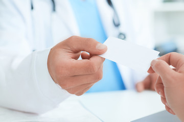 Male doctor's hand give white blank calling card to woman closeup in office. Physical, disease...