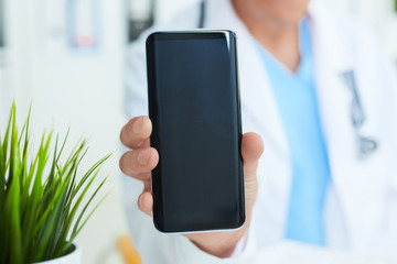Male doctor hand showing a blank smart phone screen application in hospital office background.