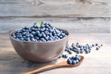 Fresh blueberries in a cup and wooden spoon on a wooden background closeup