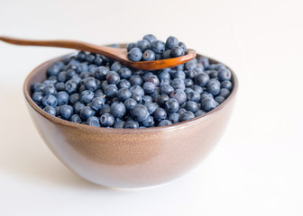 Fresh blueberries in a cup and wooden spoon on a white background closeup