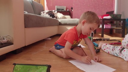 the little boy draws on paper, on the floor.