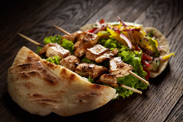 Pita stuffed with chicken, vegetables and kebab on wooden background, shallow depth of field, blurred.