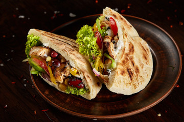 Pita stuffed with chicken, beans and letucce on clay plate over wooden background, side view, selective focus.