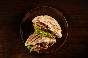 Pita stuffed with chicken, beans and letucce on clay plate over wooden background, top view, selective focus.