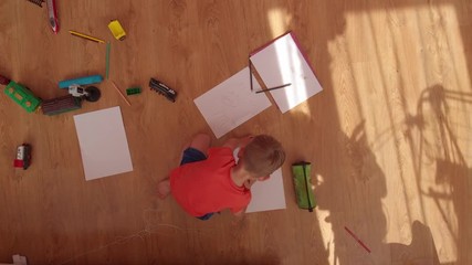 the little boy draws on paper, on the floor.
