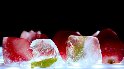 Frozen strawberries and mint leaves in ice cubes, smoke, black background.
