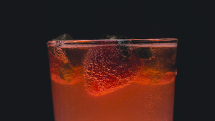 Orange alcohol cocktail in a glass, black background, strawberry, lime, black background, cold drink, ice, fresh.