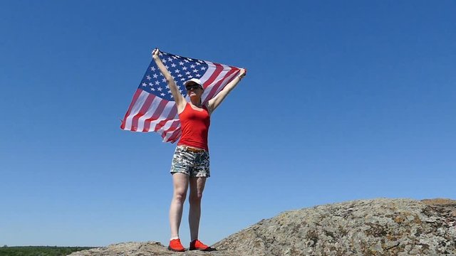 Woman  in red undershirt  stand witn American flag and look afar. Slow motion