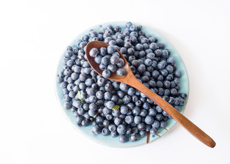 Fresh forest blueberries on a blue plate on a white background close up, top view.