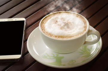 Hot coffee and mobile on wooden table that has a dark evening. There is a warm atmosphere