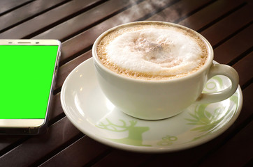 Hot coffee and mobile on wooden table that has a dark evening. There is a warm atmosphere