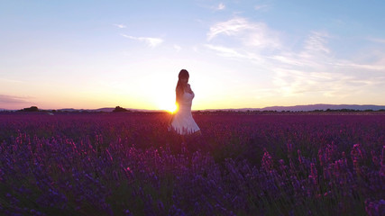 Fototapeta na wymiar AERIAL: Young woman walking trough gorgeous lavender rows at sunset in Provence