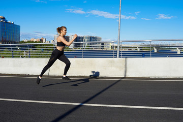 Fototapeta na wymiar Freeze action shot of self determined serious young European woman athlete running fast along stadium track, preparing for marathon on sunny spring day, dressed in stylish black leggings and top