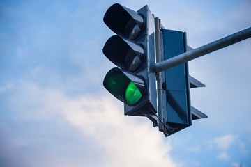 The green streetlight signal with cloudy blue skies in the background