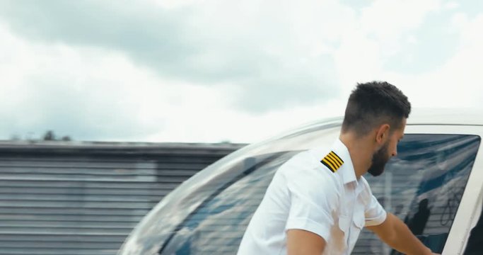 TRACKING commercial pilot in uniform greeting clients near small private helicopter on a landing point. 4K UHD