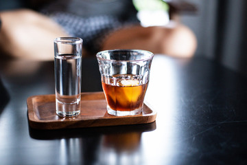 Closeup glass of water and glass of cold coffee on wooden tray,blurry light around.