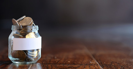 Coins in a glass jar on a wooden floor. Pocket savings from coin