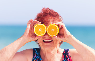 funny portrait of mature woman, grandma having fun with orange eyes on summer vacation
