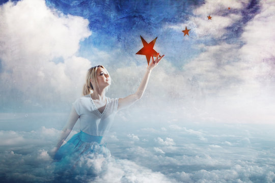 Young attractive woman Sitting on a cloud reaching for the star. Take a star from the sky, dreams and plans, concept