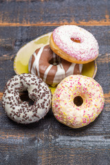 Colorful sweet glazed donuts from bakery on black wooden background close up