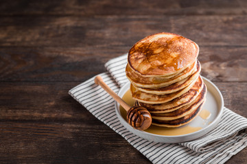 Stack of homemade pancakes with honey on rustic wooden background, copy space