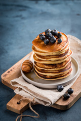 Stack of homemade pancakes with fresh blueberries and honey on blue background