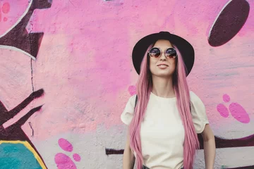 Fotobehang Happy stylish young hipster woman with long pink hair, hat and sunglasses on the street. © fedorovacz