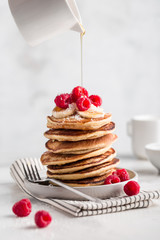 Stack of homemade pancakes with fresh raspberries and poured maple syrup on light concrete background, copy space