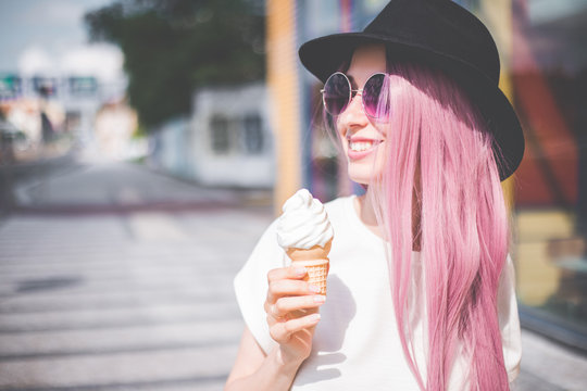 Happy Young Hipster Woman With Long Pink Hair, Hat And Sunglasses Eating Ice Cream Outdoors