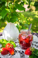 Strawberry jam and juicy ripe strawberries on a wooden table in the garden on a summer sunny afternoon in a rustic style, the concept of gardening, healthy organic vitamin nutrition