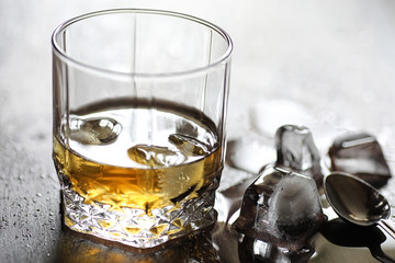 Whiskey in a glass and pieces of ice on a wood