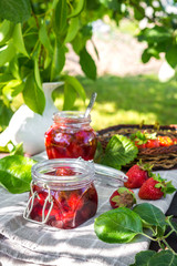 Strawberry jam and juicy ripe strawberries on a wooden table in the garden on a summer sunny afternoon in a rustic style, the concept of gardening, healthy organic vitamin nutrition