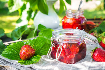 Strawberry jam and juicy ripe strawberries on a wooden table in the garden on a summer sunny afternoon in a rustic style, the concept of gardening, healthy organic vitamin nutrition