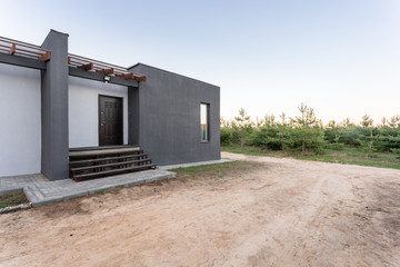 Side view of an open veranda in front of a modern forest cottage. Pine young forest under the...
