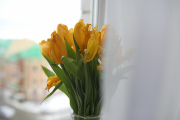 A bouquet of yellow tulips in a vase on the windowsill. A gift t