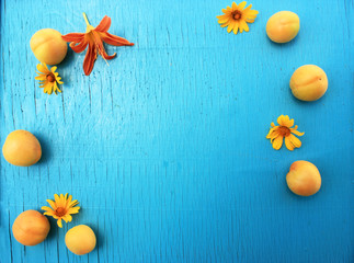 Ripe fresh apricots on a wooden turquoise table close-up with bright summer flowers. Horizontal view from above. Copy space