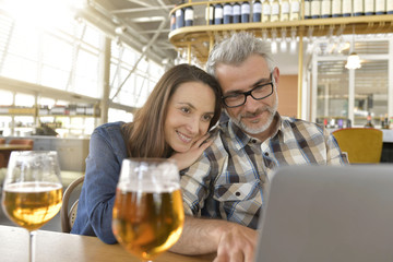 Couple in bar connected on laptop computer, having a drink