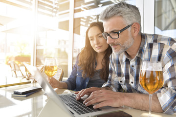 Couple in bar connected on laptop computer, having a drink