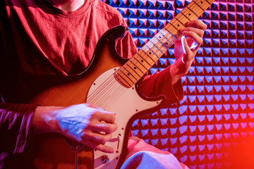 Young man playing on the guitar in sound recording studio.