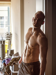 Handsome muscular shirtless young man standing in a gym, looking at camera, leaning on open door