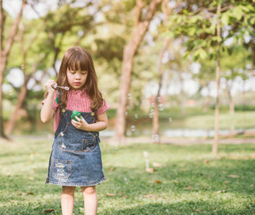 A little girl blowing soap bubbles in summer park