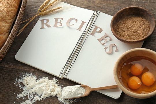 Notebook with word RECIPES and ingredients for making bread on table