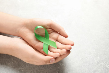 Woman holding green ribbon on grey background. Cancer awareness