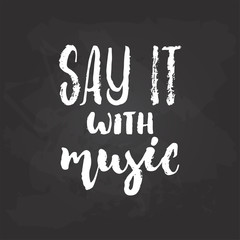 Fototapeta na wymiar Say it with Music - hand drawn Musical lettering phrase isolated on the black chalkboard background. Fun brush chalk vector quote for banners, poster design, photo overlays.