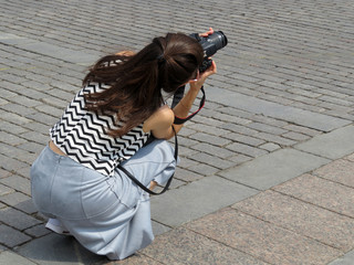 Girl photographer with camera taking pictures squatting on the street. Woman tourist