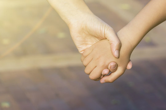 Close up of mother or older sister and a child hands at the sunset with copy space.