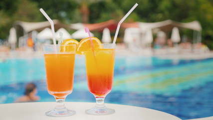 Two exotic cocktails on the background of bathing tourists in the pool in a large comfortable hotel
