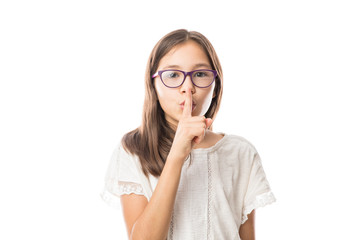 Beautiful little girl putting finger up to lips & ask silence on white background